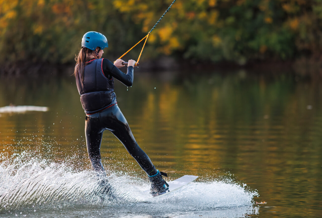 Girl on a wakeboard. An athlete performs a trick on the water. Autumn Park. Travel Vest.